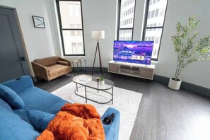 Ein modernes Wohnzimmer mit einem blauen Sofa, einem Couchtisch, einem Fernseher und einer Topfpflanze.