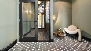 A hotel lobby with a patterned floor, a modern chair, and a door leading to another room. - Urban 1BR Downtown–Close (Pittsburgh)