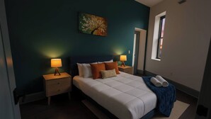 A bedroom with a bed, two bedside tables with lamps, a painting on the wall, and a window. - Urban 1BR Downtown  –Close (Pittsburgh)