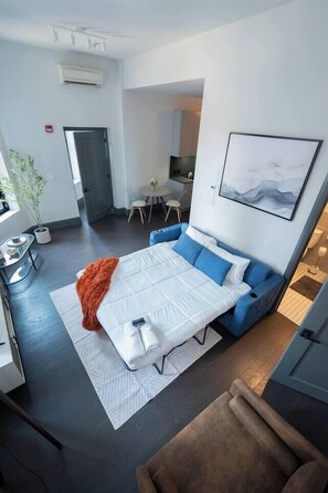 Ein modernes Hotelzimmer mit Bett, einer Couch, einem Essbereich und einer Küche im Hintergrund.