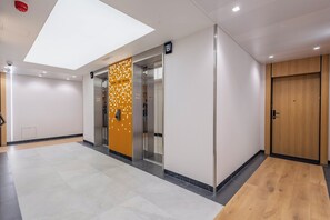 Ein moderner Aufzug mit digitaler Anzeige, einer Holztür und einer Wand mit geometrischem Muster.