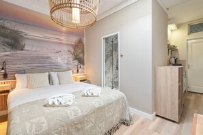 Un dormitorio con una cama grande, una mesita de noche, una lámpara, una obra de arte en la pared y una puerta que da a un baño.