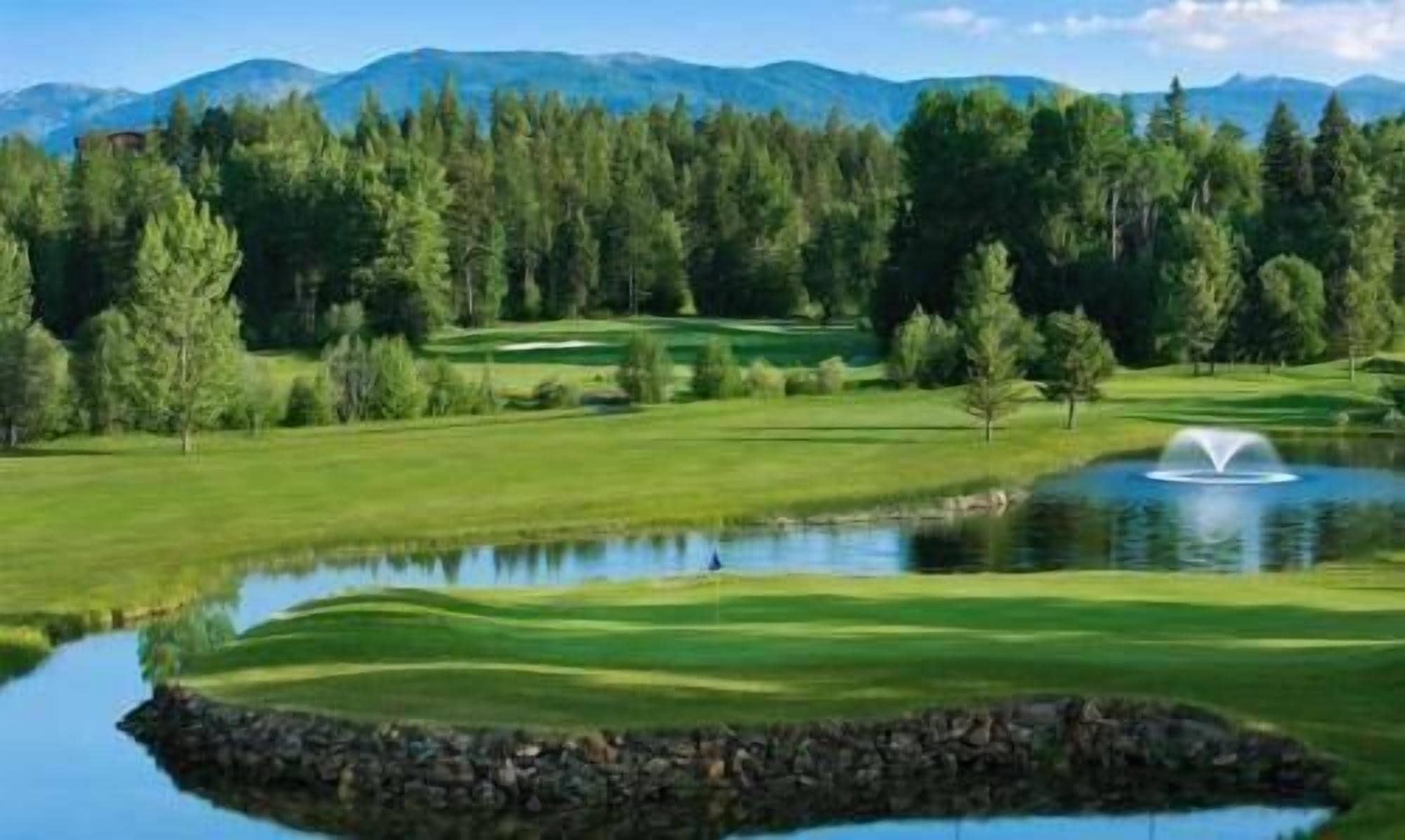 Ein Golfplatz mit Teich, Bäumen und Bergen im Hintergrund.