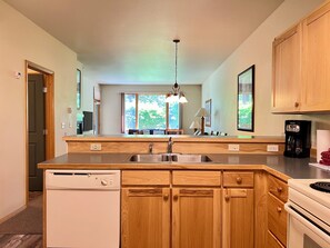 A modern kitchen with wooden cabinets, a built-in dishwasher, a coffee maker, and a large window providing natural light. - Meadow Lake Private Timeshares (Columbia Falls)
