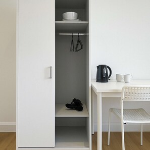 Ein weißer Kleiderschrank mit Ablagefläche, Kleiderstange und einem Paar Schuhen auf dem Boden.