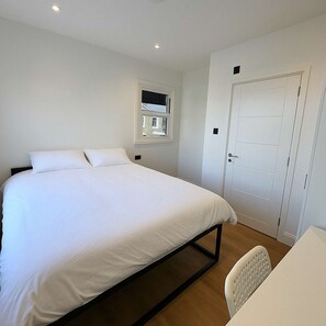 Ein Schlafzimmer mit Bett, Fenster, Tür und einem Sessel.