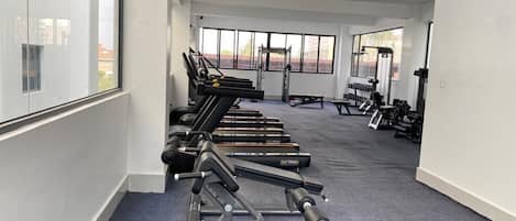 Un gimnasio con equipamiento de ejercicio, amplias ventanas y piso alfombrado.