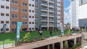 Un hotel de varios pisos con balcones, una terraza en la azotea y un patio con césped.