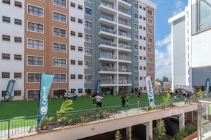 A multi-story hotel with balconies, a rooftop terrace, and a grassy courtyard.