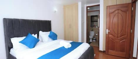 Una habitación de hotel con una cama grande, una puerta de madera y un baño visible al fondo.