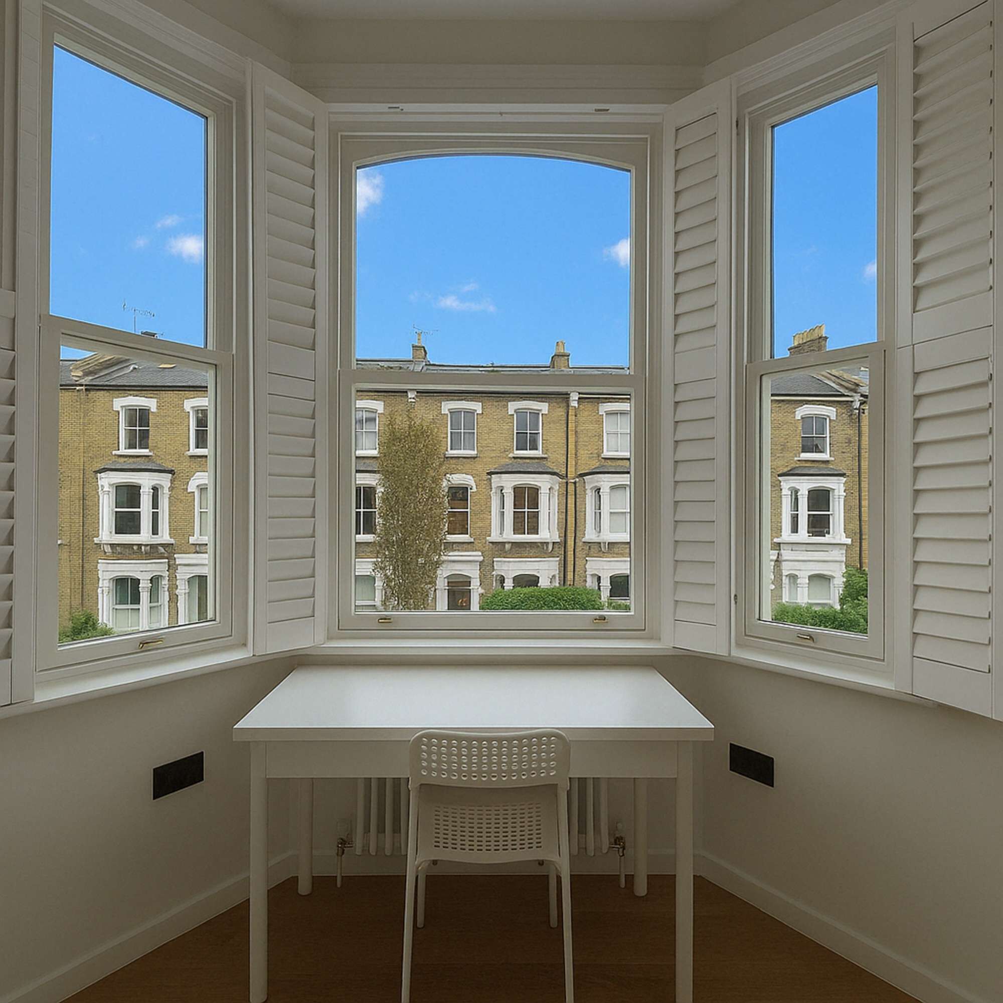 A corner room with a bay window overlooking a row of terraced houses.