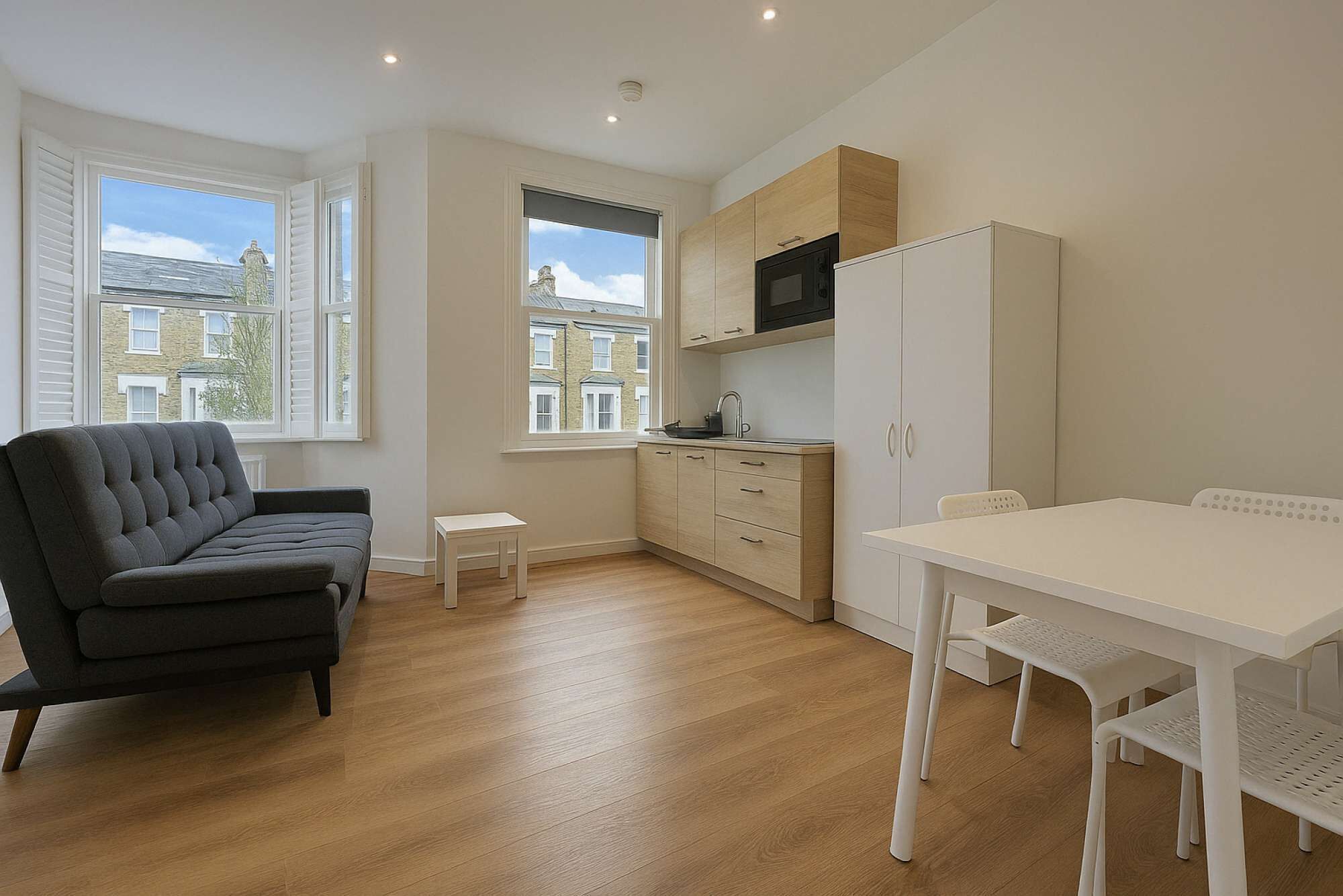 A modern kitchen with wooden cabinets, a dining table with chairs, and a grey sofa.