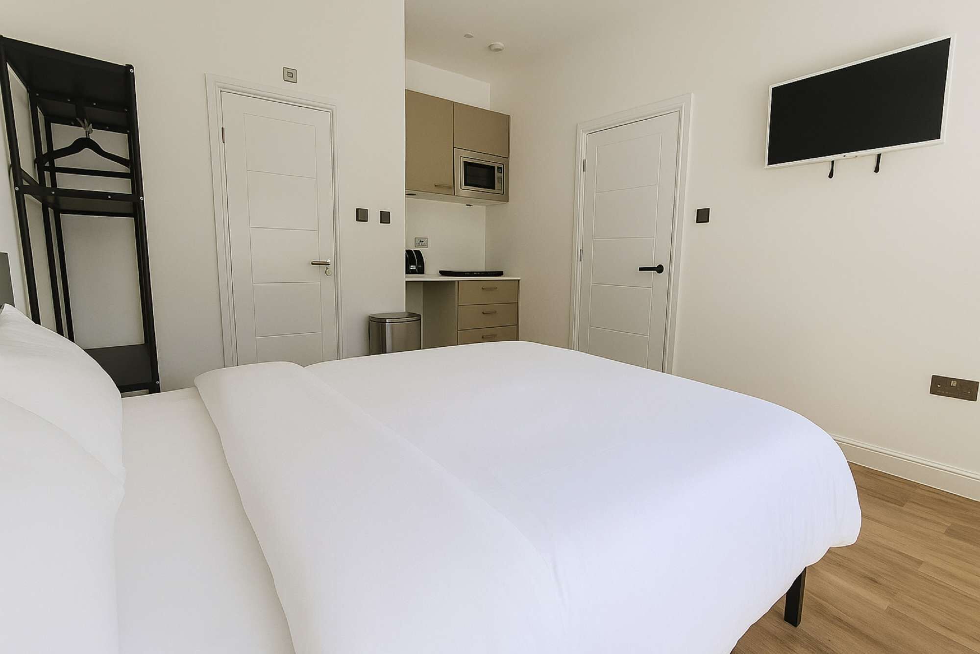 A hotel room with a large bed, a TV mounted on the wall, and a kitchenette area.