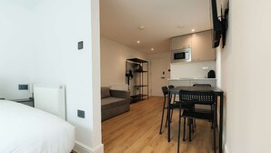 Ein Hotelzimmer mit einem Bett, einem Sofa, einem Esstisch mit Stühlen, einer Mikrowelle und einem an der Wand befestigten Fernseher.