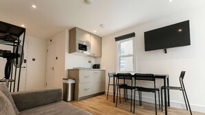 Ein kompakter Wohnraum mit Küchenzeile, einem Essbereich mit Stühlen, einer Couch und einem an der Wand befestigten Fernseher.