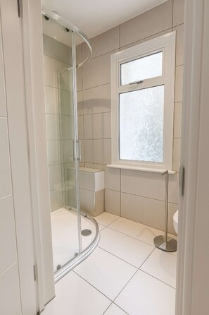 A modern bathroom with a glass-enclosed shower, a toilet, and a window. - Large Studio | Private Bathroom & Kitchenette NW10 (Greater London)