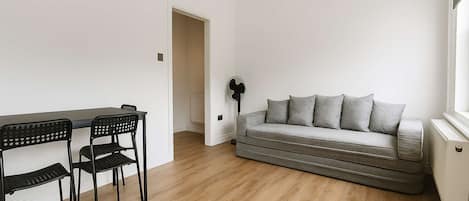 A room with a dining table and chairs, a sofa, and a radiator.