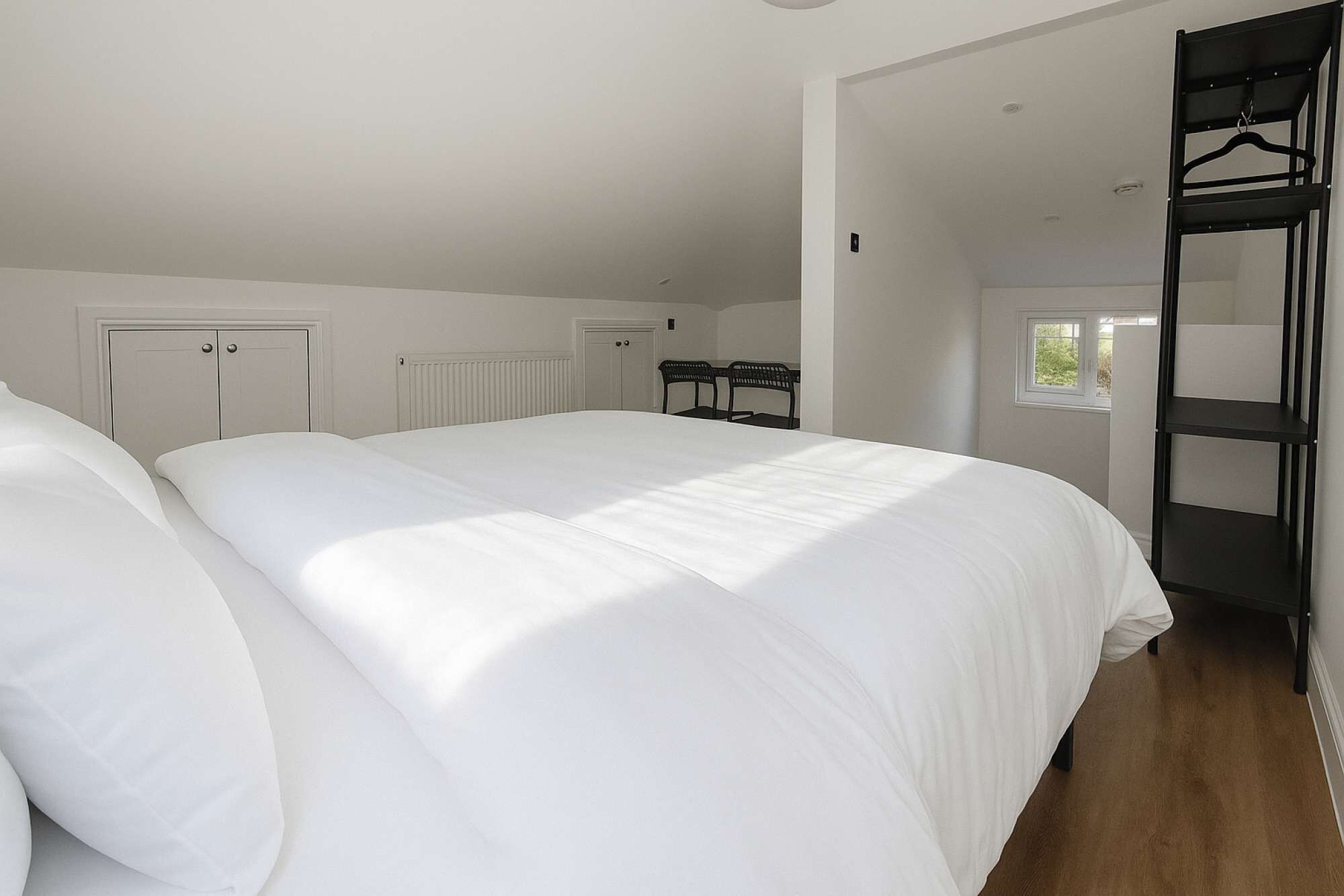 A bedroom with two beds, a radiator, a window, and a black metal shelf.
