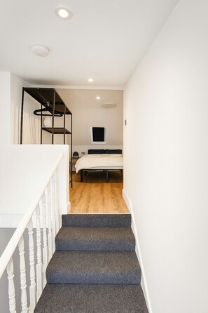 Eine Treppe führt zu einem Schlafzimmer mit Bett, Fernseher und Kleiderschrank.