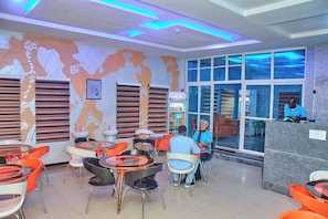 Rebedor d'hotel amb un mural de mapa mundial, una taquilla d'informació i una zona d'estar amb taules i cadires.