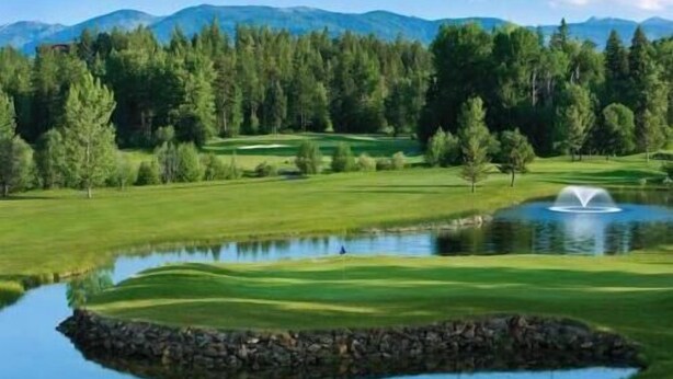 Een golfbaan met een vijver, bomen en bergen op de achtergrond.