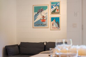 Ein Zimmer mit weißer Wand, einem dunkelgrauen Sofa und drei gerahmten Postern mit Berglandschaften.