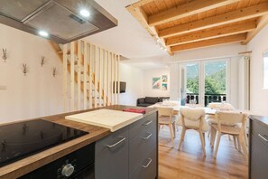 A modern kitchen with a wooden island, a dining area with a table and chairs, and a balcony with a view of the outdoors. - Napoléon - Cosy 80m² Duplex | Central | Sleeps 6 | Parking (Les Houches)