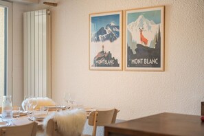 Ein Essbereich mit einem Tisch für zwei Personen, zwei gerahmte Poster an der Wand und einem Fenster mit Jalousien.