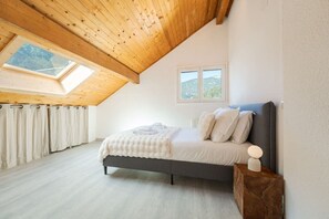 Ein Schlafzimmer mit Oberlicht, einem Bett mit Kissen, einem Nachttisch mit Lampe und einem Fenster mit Blick.