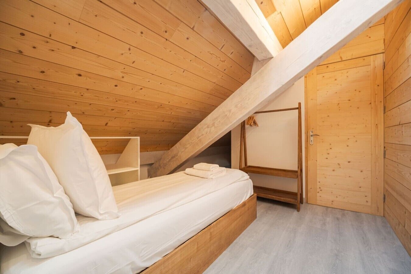 Une petite pièce en bois, avec un toit en pente, comprenant un lit simple, une armoire en bois et une petite étagère.