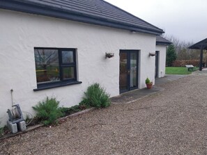 A white building with black-framed windows and a door, a gravel driveway, and a wheelbarrow in the background. - House Sleeps 11 With Parking (Tralee)