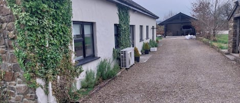 A gravel driveway leading to a building with a stone wall partially covered in ivy.