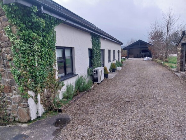 A gravel driveway leading to a building with a stone wall partially covered in ivy.