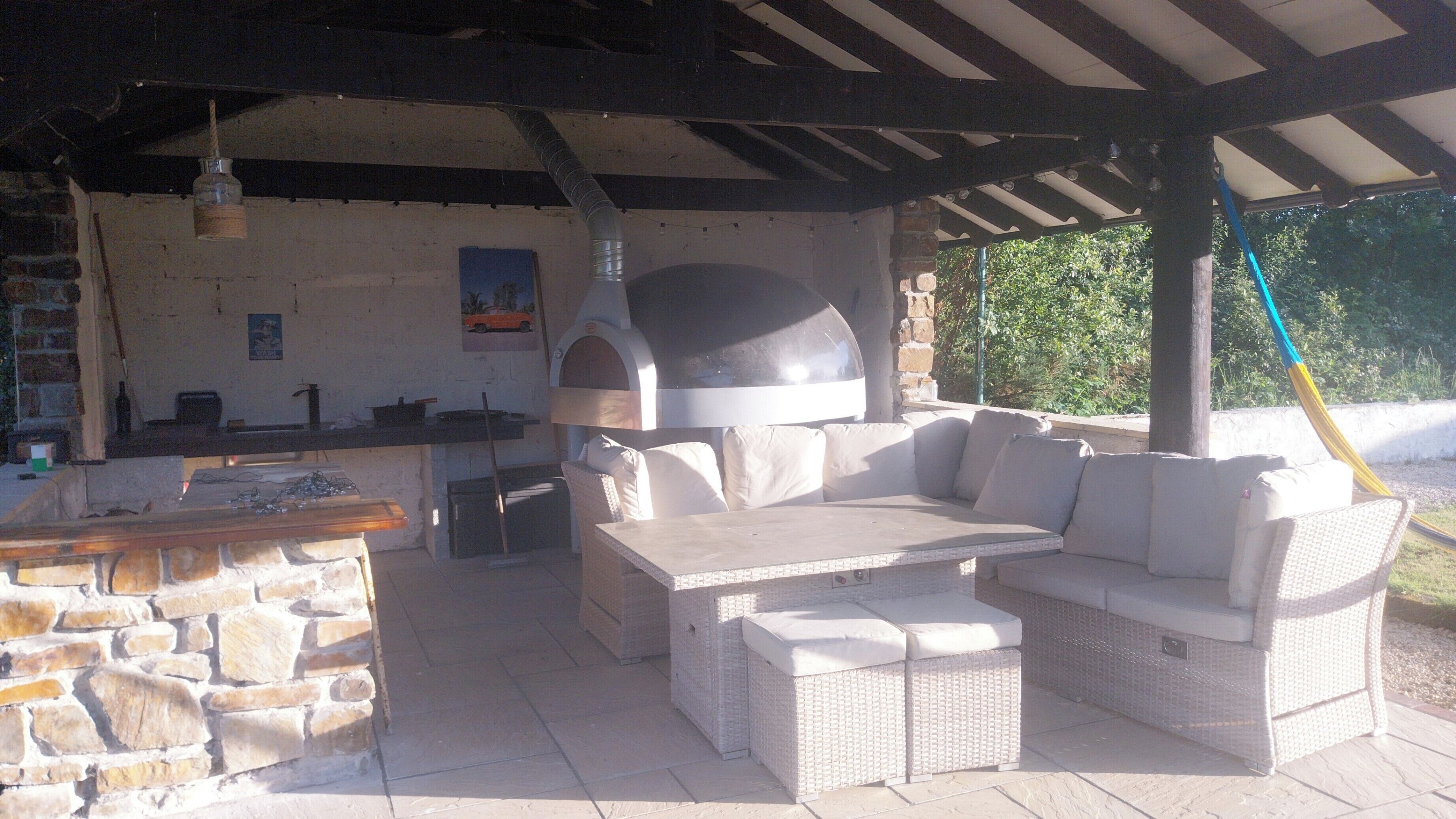 An outdoor patio with a stone wall, a bar area, and a large pizza oven.