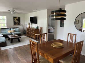 A modern living room with a dining area, a flat-screen TV mounted on the wall, and a ceiling fan. - Bountiful Bokeelia-Secluded 3 fenced tropical acres-pet friendly (Bokeelia)