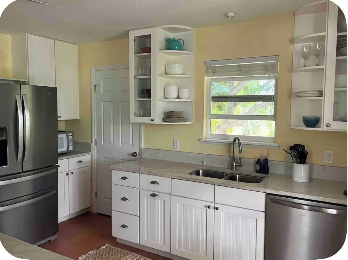 A kitchen with white cabinetry, a stainless steel refrigerator, a microwave, and a window with a view of greenery.