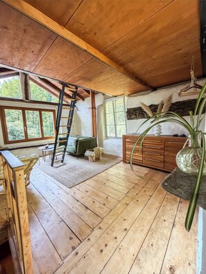 A rustic wooden interior with a loft area, a ladder, a green sofa, a small dog, and a large plant.