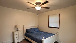 Een slaapkamer met een bed, nachtkastje, plafondventilator en een raam met zonwering.