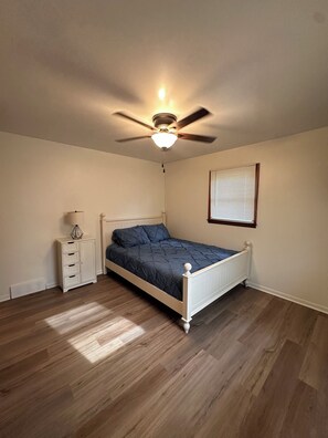 Ein Schlafzimmer mit Bett, Nachttisch, Deckenventilator und einem Fenster mit Jalousien.