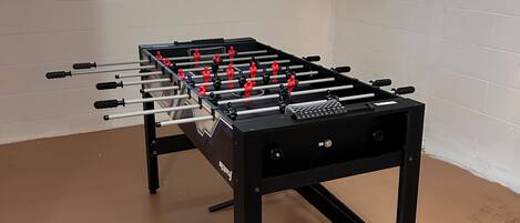 Une table de baby-foot dans une pièce aux murs blancs et dotée d’une fenêtre.