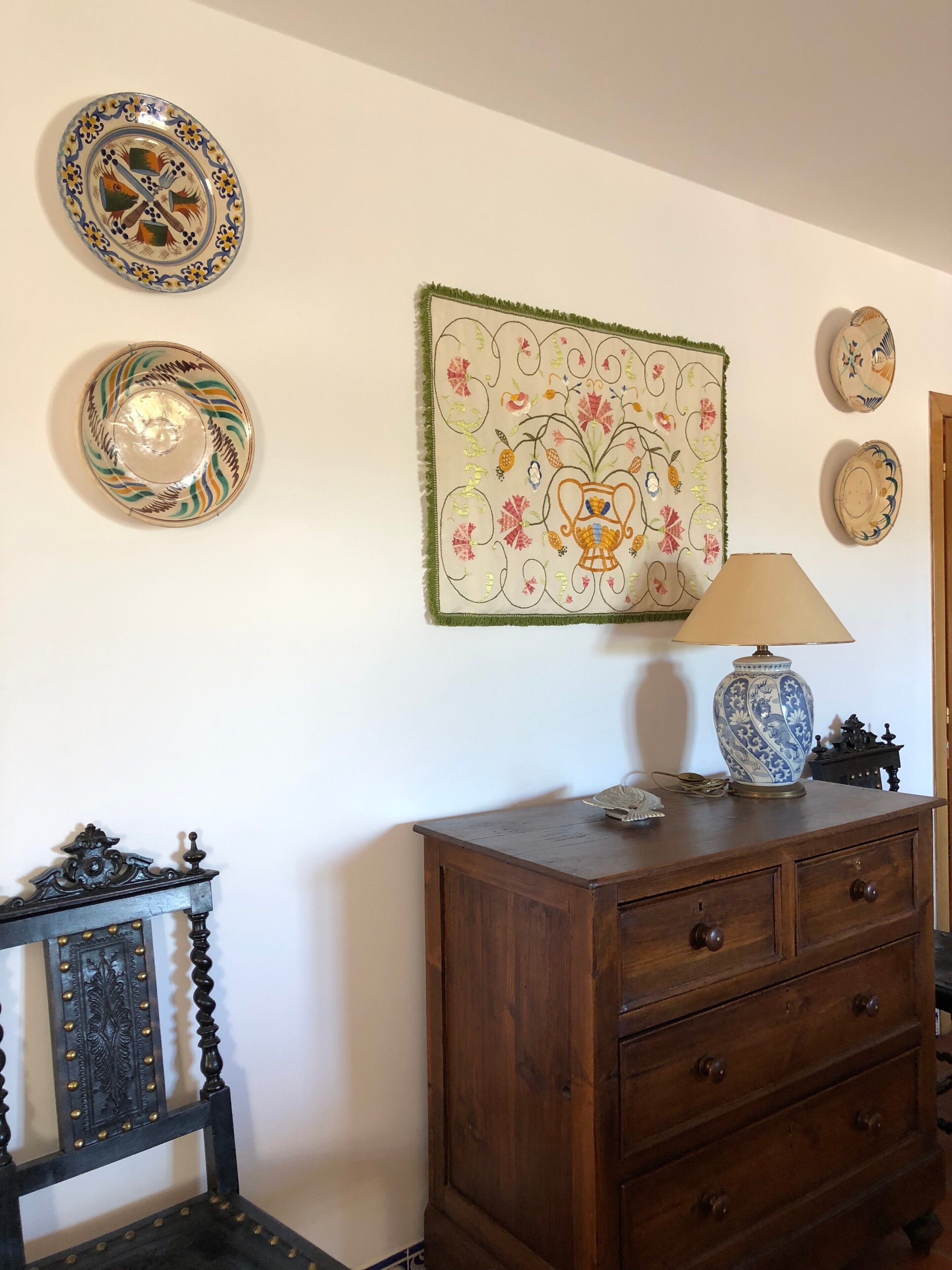 Une pièce comprenant une commode en bois, une chaise, ainsi que des assiettes décoratives et une tapisserie accrochées au mur.