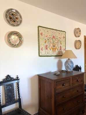 A room with a wooden dresser, a chair, and wall-mounted decorative plates and a tapestry.