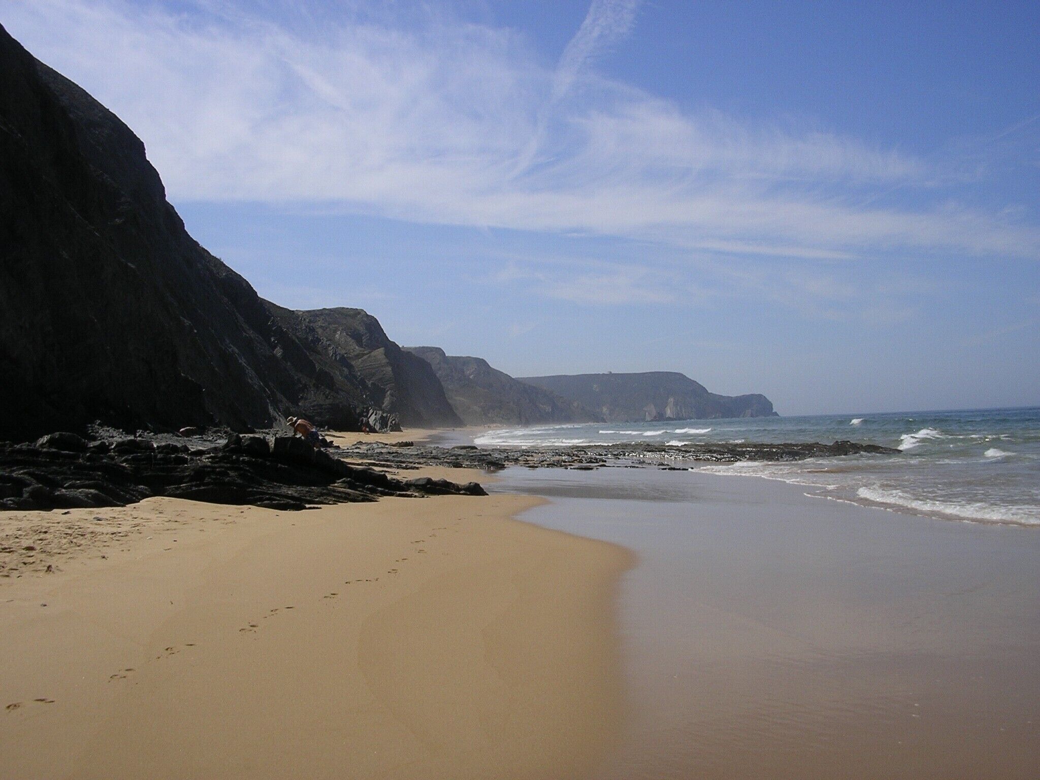 A beach with a sandy shore, rocky cliffs, and waves.