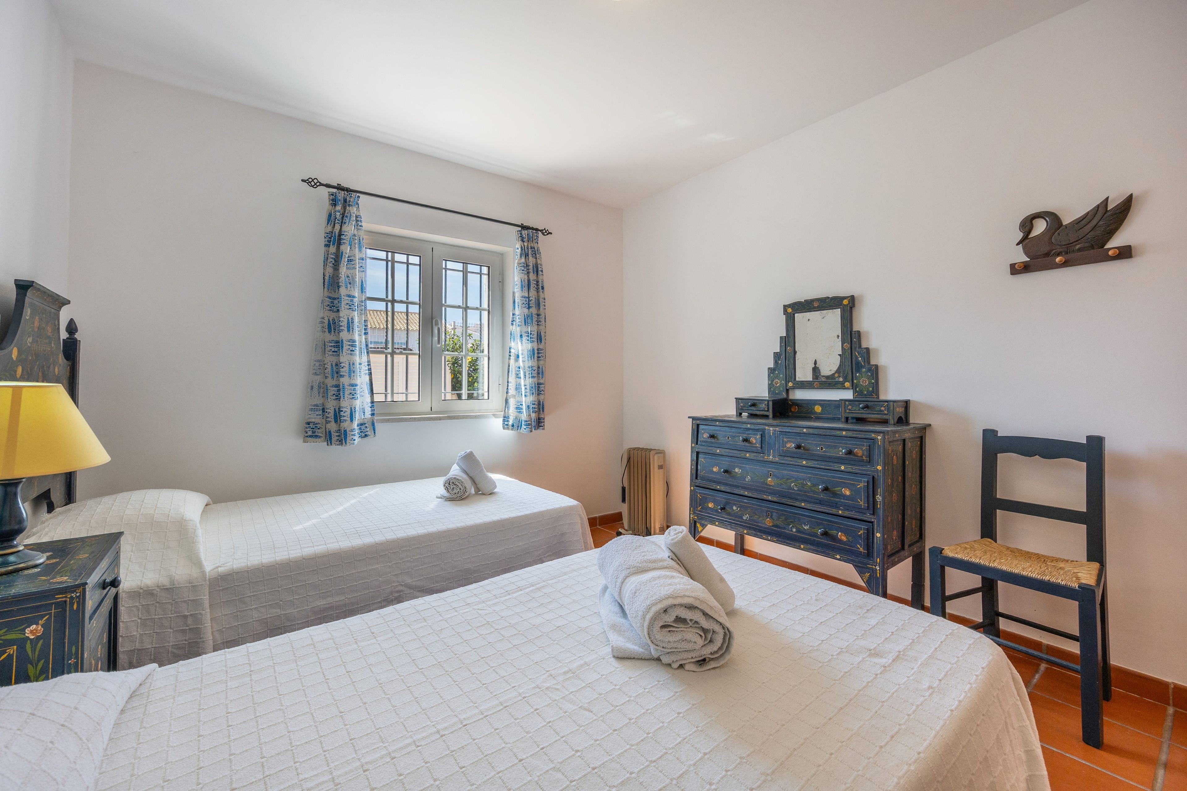 Een slaapkamer met twee bedden, een dressoir, een stoel, een spiegel en een raam met gordijnen.