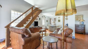 Un salon spacieux avec un escalier en bois, des canapés en cuir, une table basse et un lampadaire.