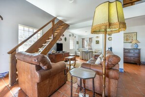 Ein geräumiges Wohnzimmer mit einer Holztreppe, Ledersofas, einem Couchtisch und einer Stehlampe.