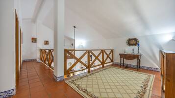 Une pièce mansardée spacieuse avec un plafond en pente, une rambarde en bois, un tapis à motifs et une petite table sur laquelle est posée une bougie.
