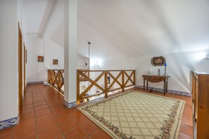Ein geräumiges Dachzimmer mit schrägen Wänden, einem Holzbalkon, einem gemusterten Teppich und einem kleinen Tisch mit Kerze.