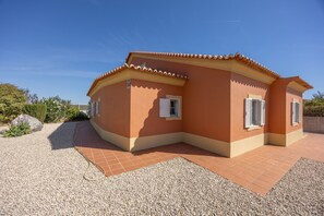 A single-story house with a curved roof, a gravel driveway, and a clear blue sky.