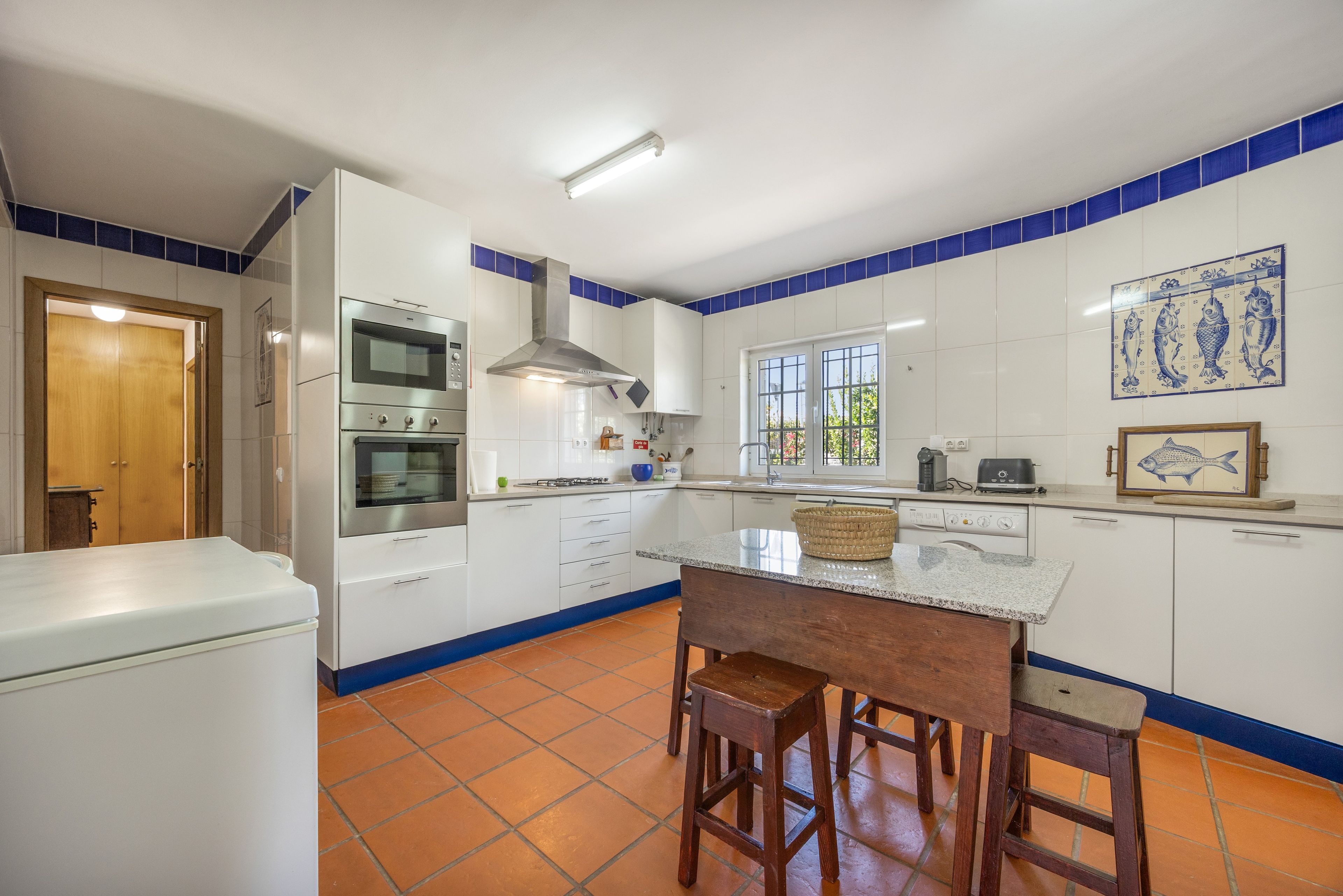 A kitchen with white cabinets, blue accents, a double oven, a gas stove, a sink, and a window.
